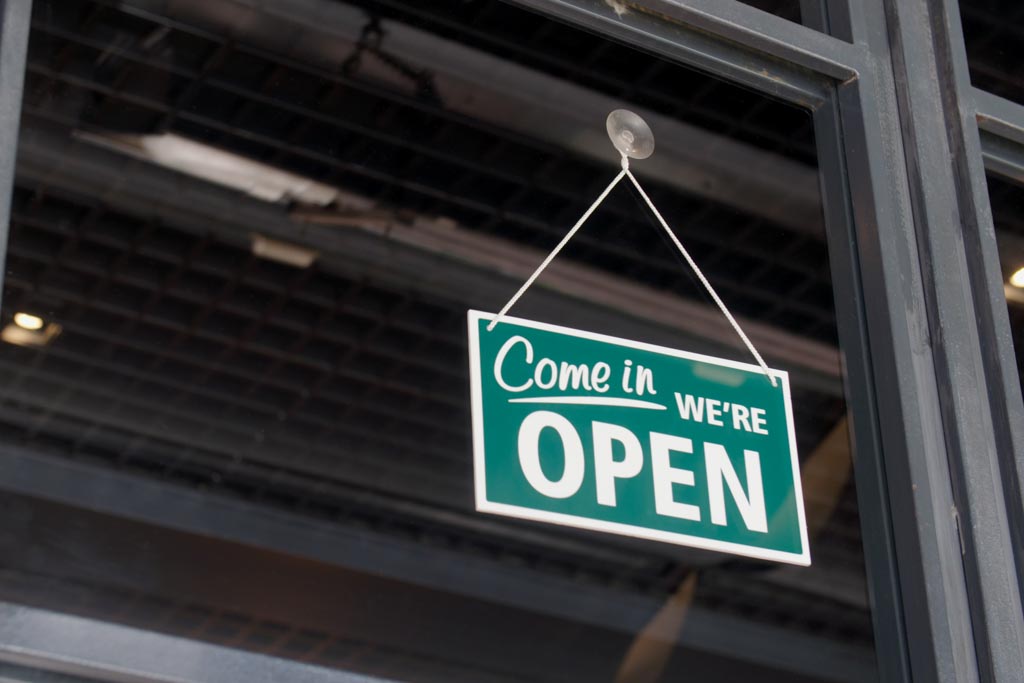 A green sign hangs in a glass window; it reads "Come in, we're open."