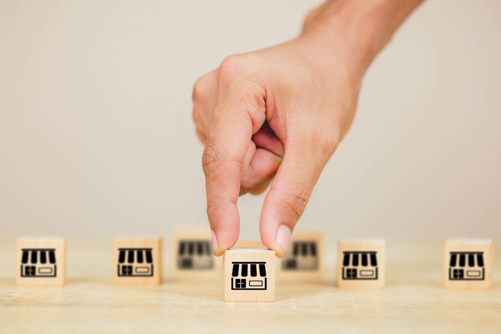 To show the concept of franchises, a finger and thumb place a small wooden block with a storefront on it in a line of identical blocks.