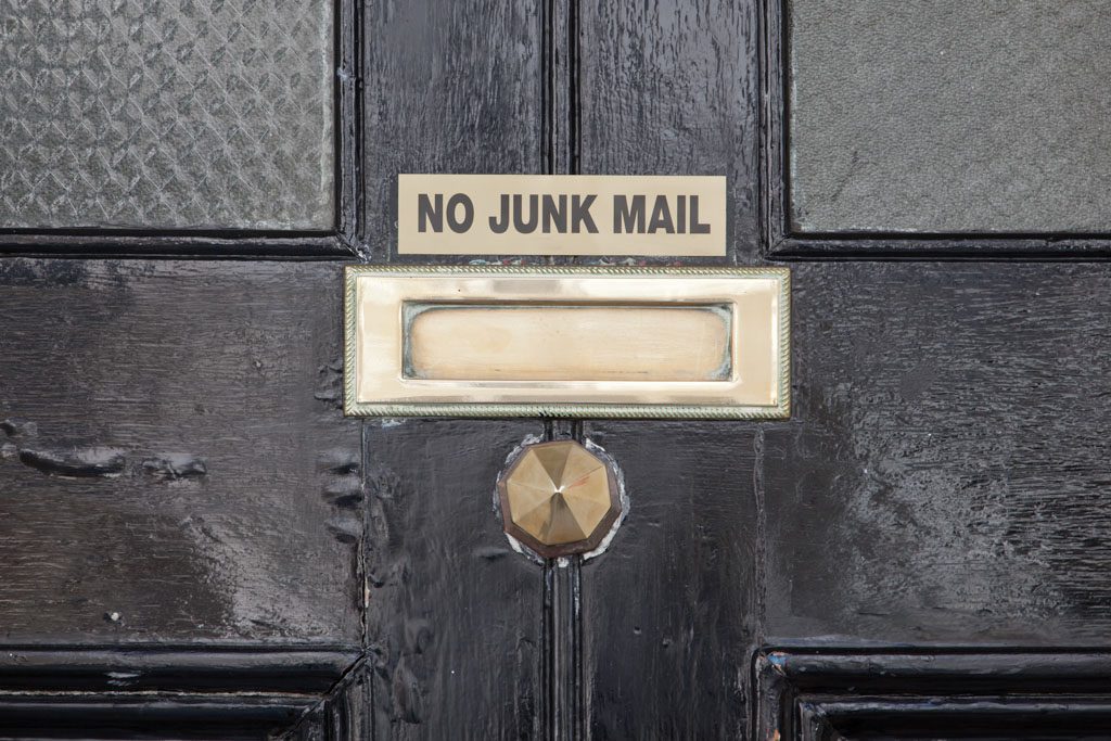 A gold mail slot in a dark wooden door with a sign that reads "no junk mail."