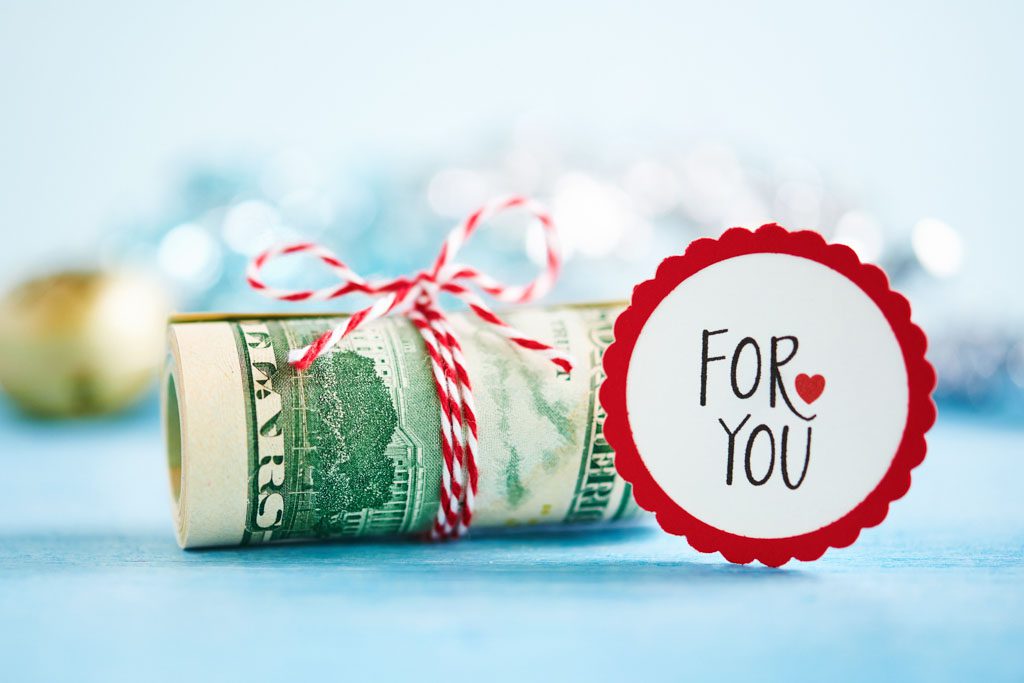 A tight roll of money is held by a bow with a red and white label that says "for you."