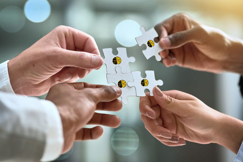 Four people in business attire reach to connect the puzzle pieces they hold.