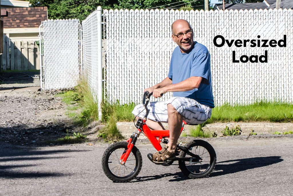 A bald adult man smiled as he rides a red bike that's far too small for him.