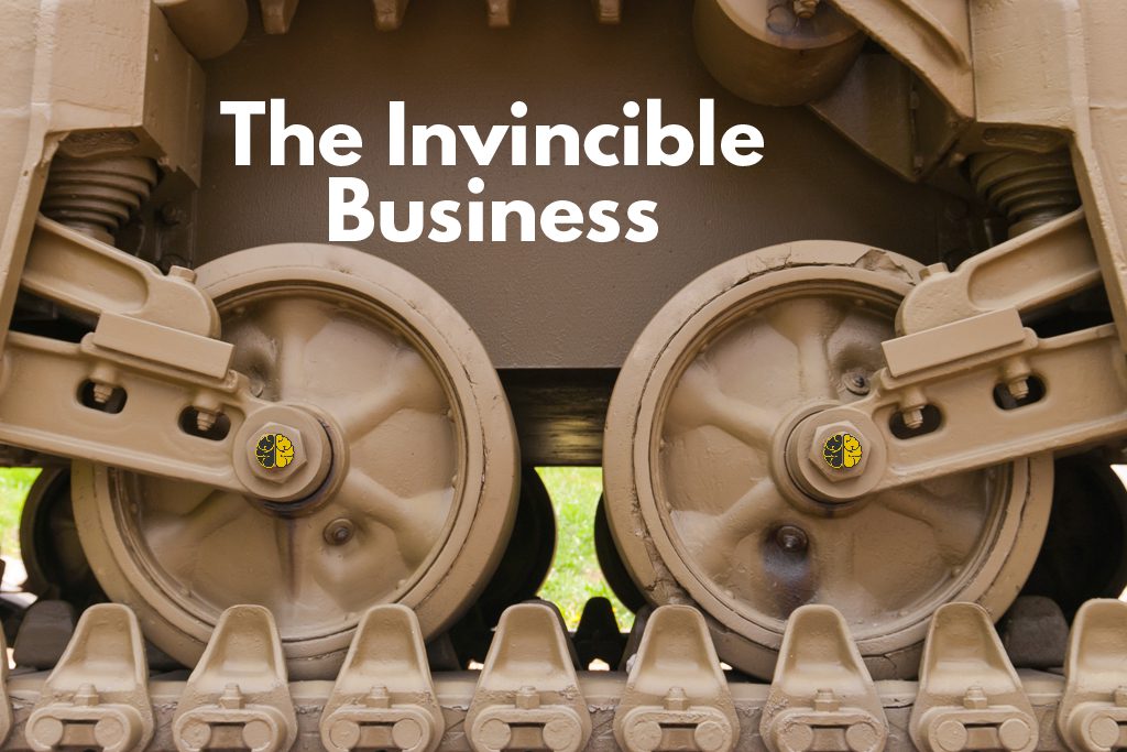 The tan wheels and tread of a powerful tank, with the words "The Invincible Business" superimposed in white.