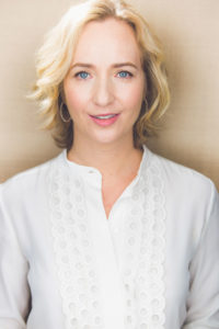 A portrait head shot of blond author Allison Schrager against a cream background.