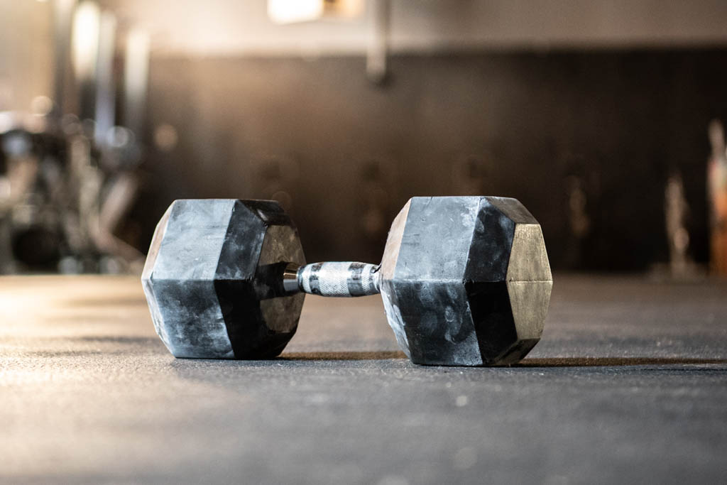 A rubber-coated hex dumbbell sits on a black rubber mat in a microgym.