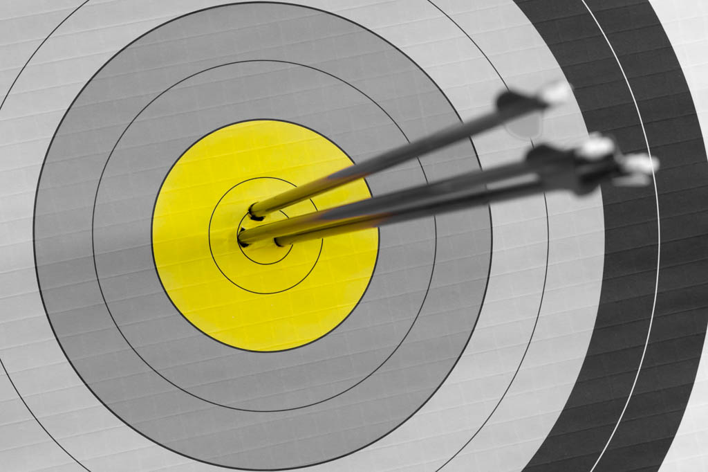 A black and white archery target with three arrows buried in a bright yellow center ring.