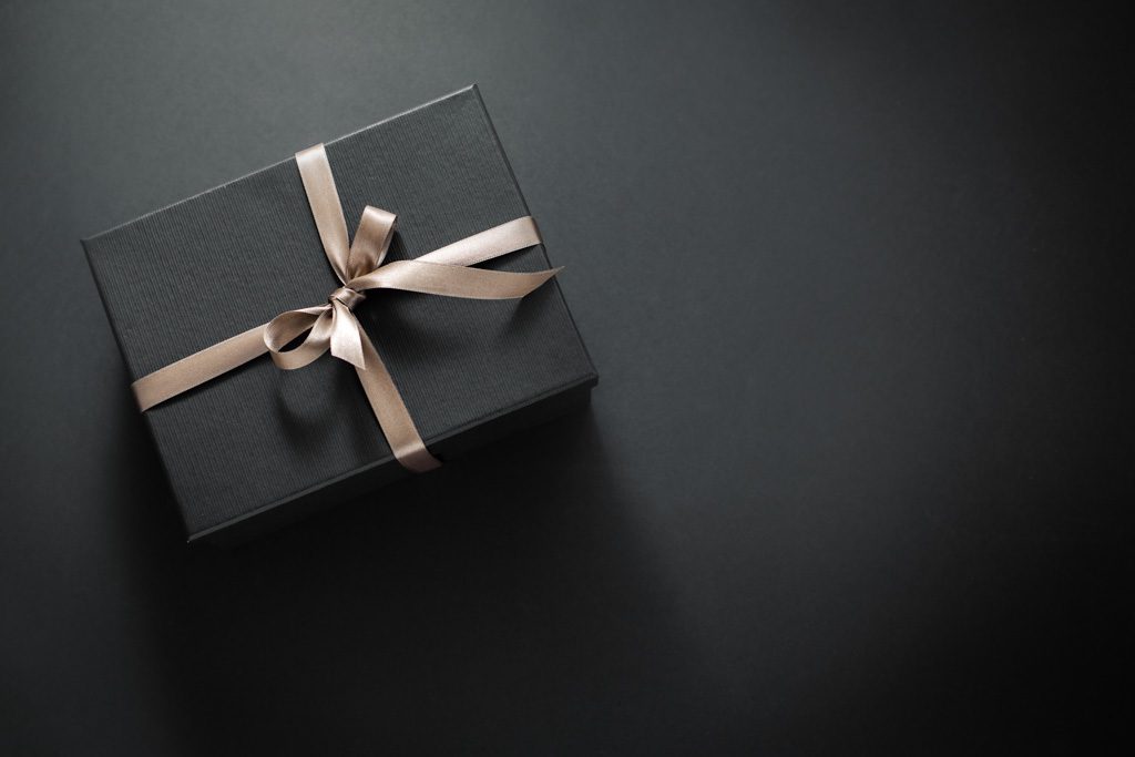 A black gift box with a pink bow sits on a black background.