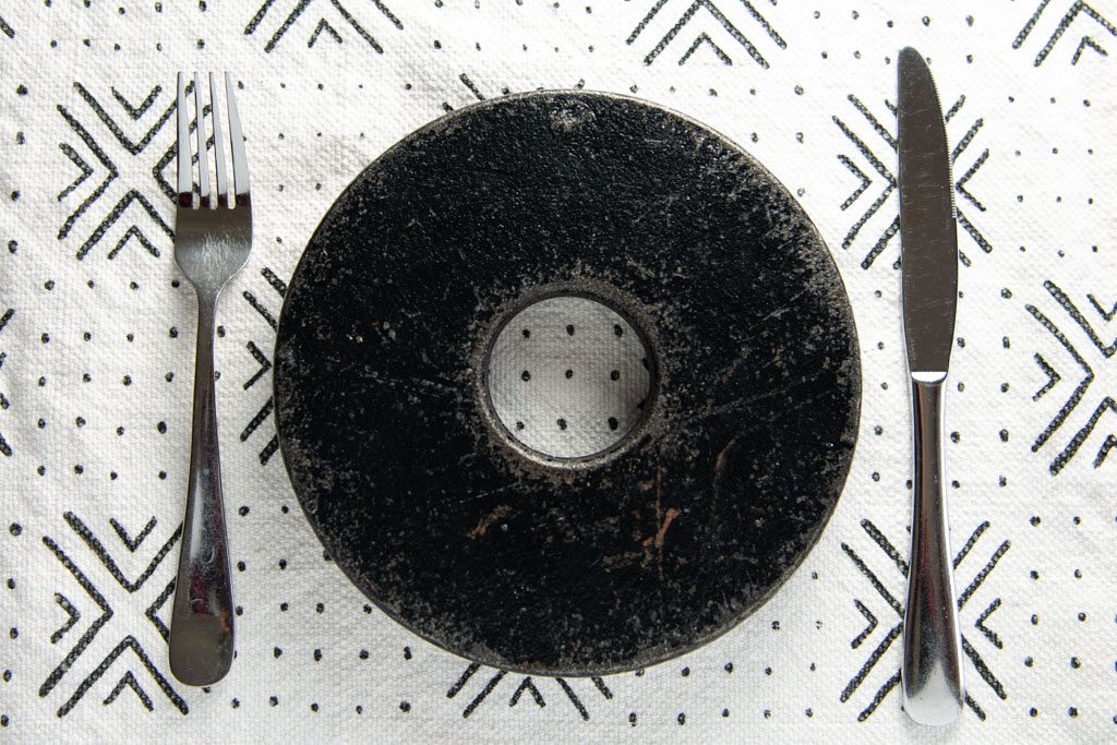 A black metal 10-lb. weightlifting plate sits on a placemat with a silver knife and fork on either side.