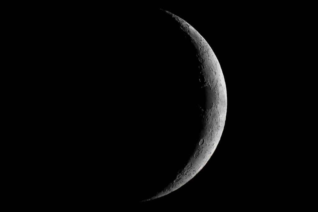 A black and white close-up image of a thin crescent of the moon.