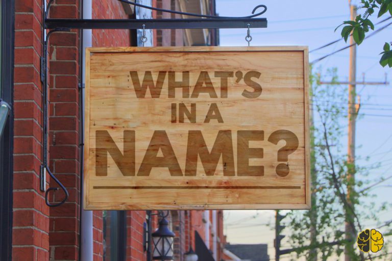 A wooden sign hanging outside a brick building inscribed 'What's In A Name?"