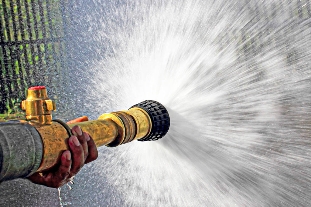 A close-up image of a fire hose with a wide spray of water coming from the nozzle.