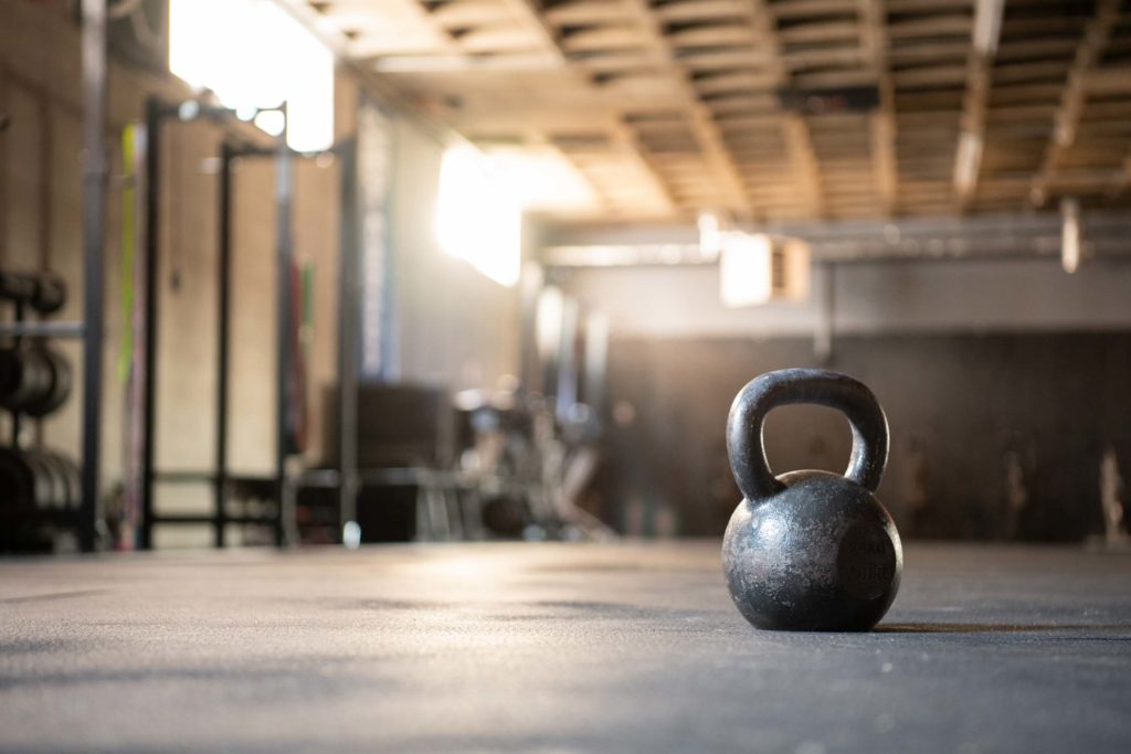A kettlebell sits on the floor of a functional training gym lit by sunlight.