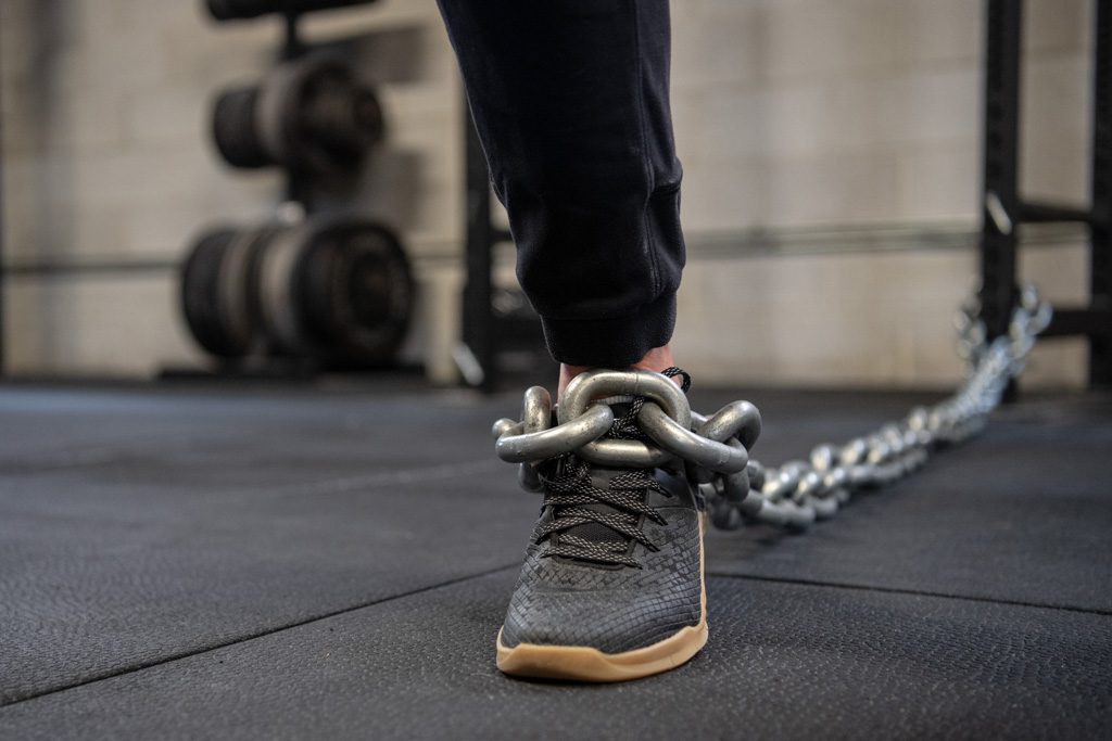 A coach's leg is chained to a squat rack to illustrate FOMO in the fitness business.