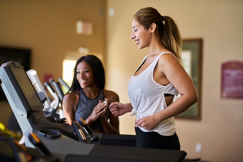 A personal trainer smiles as a client learns to use a treadmill in a fitness facility.
