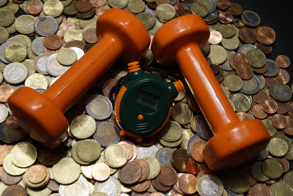 A set orange dumbbells and a stopwatch on a pile of coins.