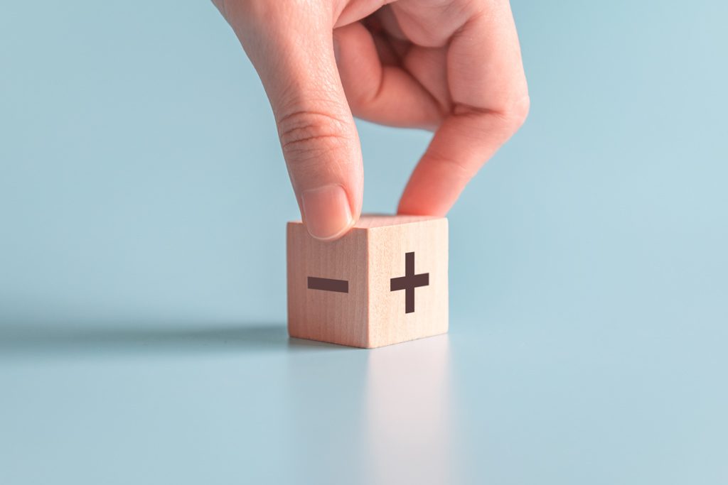A closeup of a finger and a thumb spinning a wooden block with addition and subtraction symbols on it.