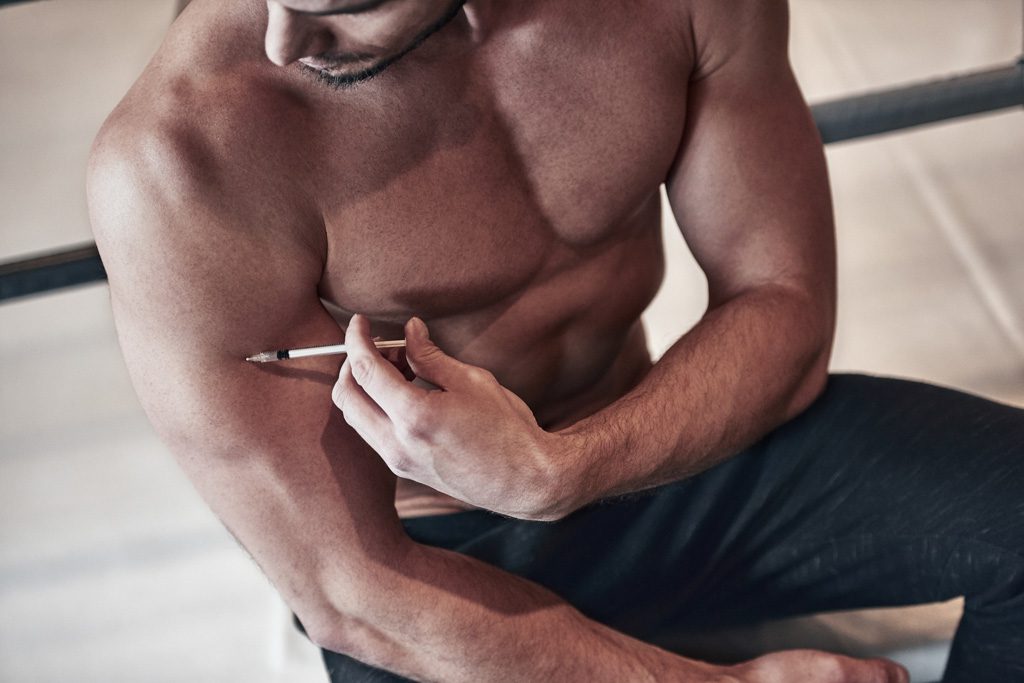 A young male athlete injects steroids into his biceps with a needle.