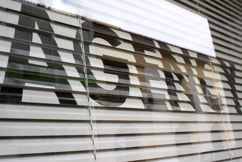 "Agency" text on a glass window of a business with Venetian blinds behind.