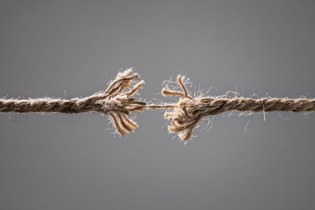 A frayed rope held together by a single strand in front of a gray background.