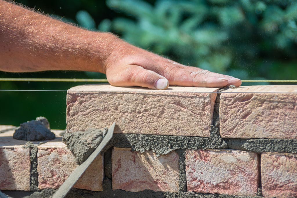 A closeup image of a man's hand as he uses mortar to lay the first row of bricks.