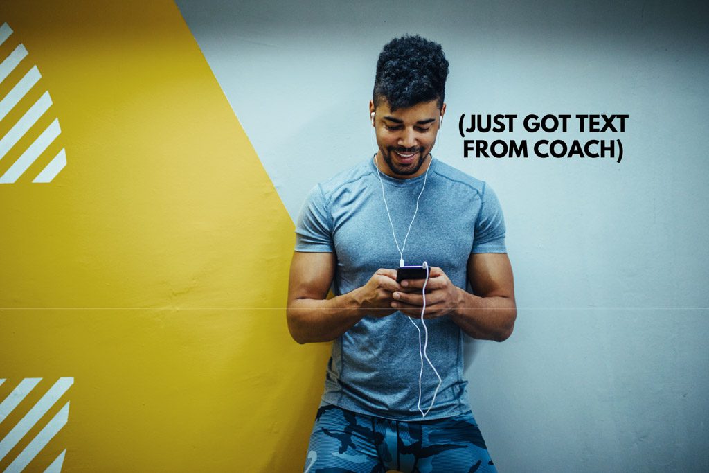 A gym client in workout wear smiles as he receives a text from a coach.