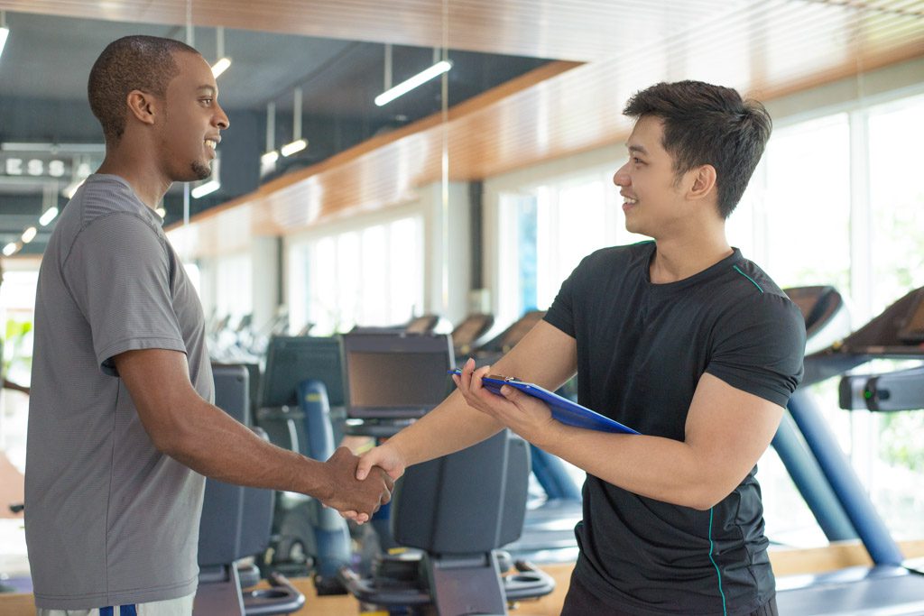 A smiling gym owner greets a prospective client with a handshake before a free consultation.