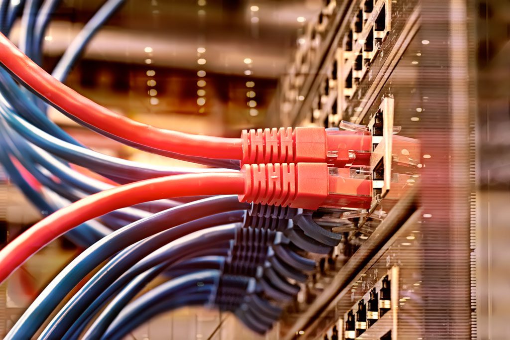 A closeup of two red ethernet cables connected to the back of a large computer.