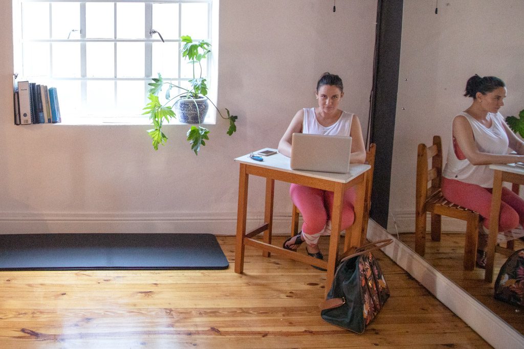 The owner of a yoga studio sits at a small desk and reviews financial statements on a laptop.