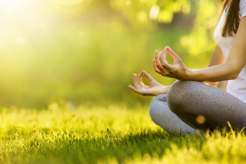 A young yogi meditates on the grass at sunset.
