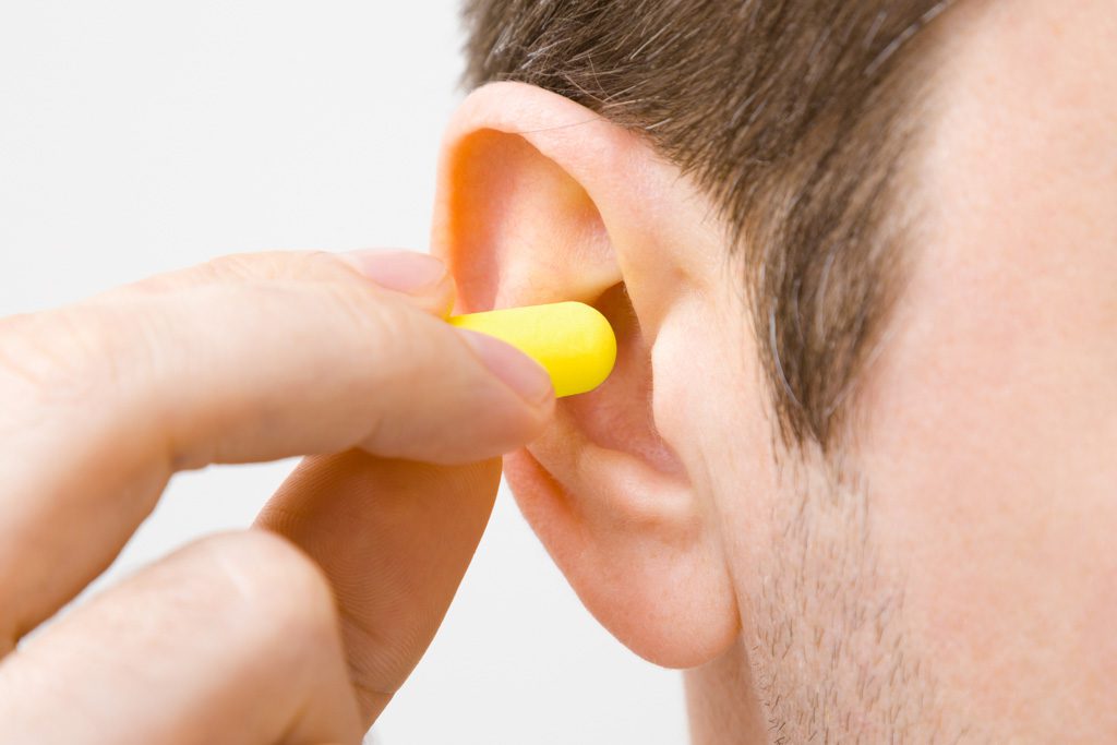 A closeup of a man placing a yellow earplug into his ear.