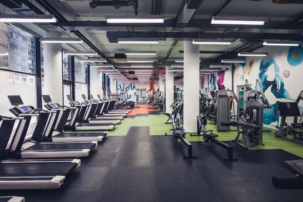 A photo of an empty gym full of treadmills and various cable stations for weight training.