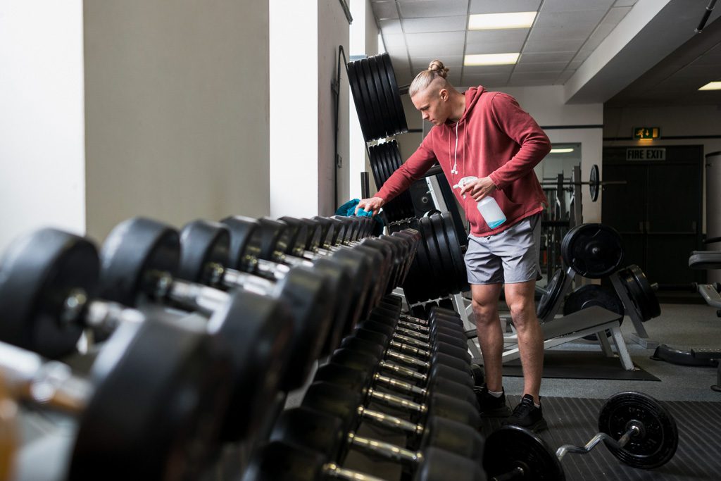 A new gym owner uses a rag and spray bottle to clean dumbbells before opening the gym.