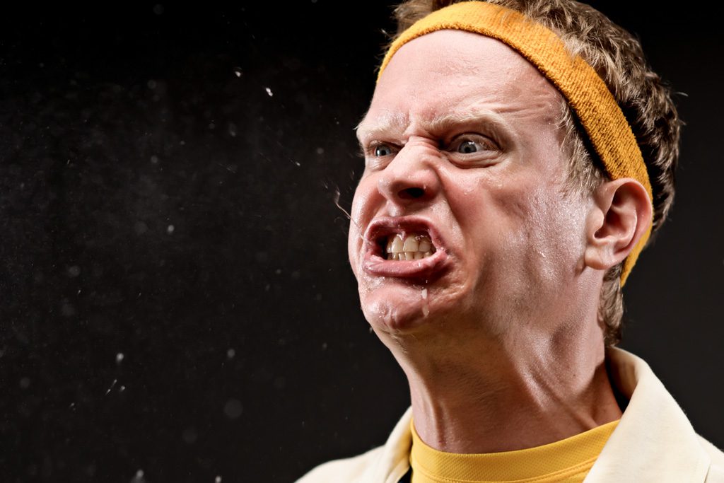 An angry gym owner in a yellow headband screams in frustration.