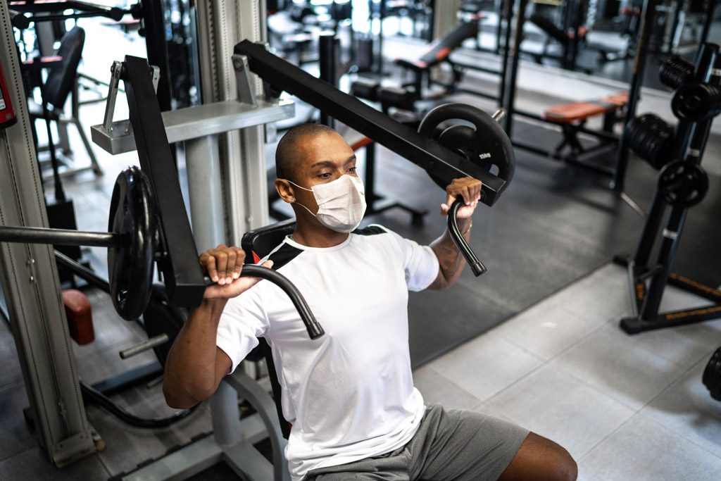 A male does shoulder presses in a facemask to illustrate the changes described in this fitness industry analysis.