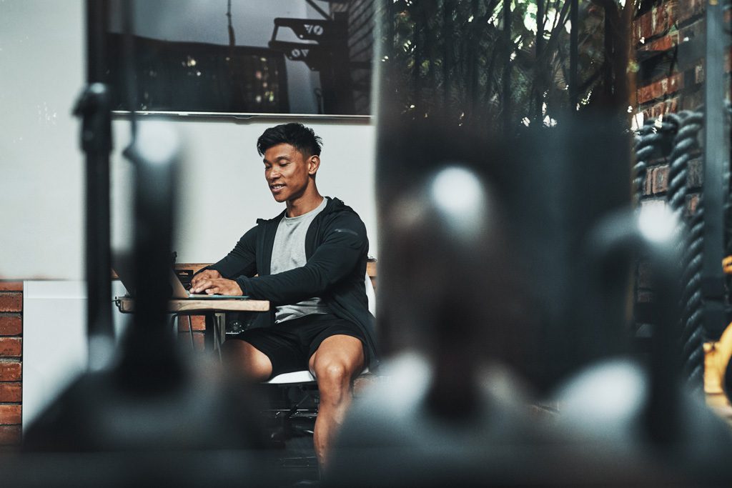A gym owner sits at a laptop and writes a fitness blog.