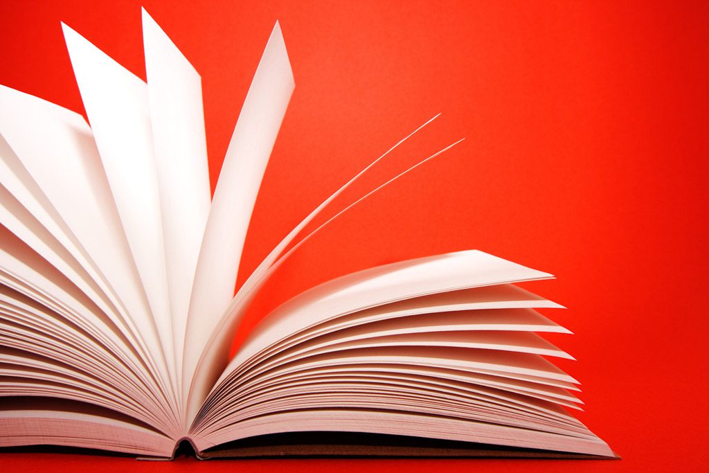 A closeup of the pages of a thick book open against a red background.