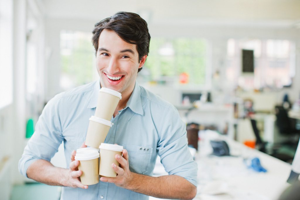 A smiling man exists a coffee store carrying for paper cups of java.
