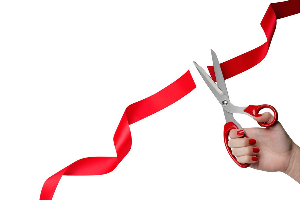 A hand with scissors cuts red tape at a gym grand opening.