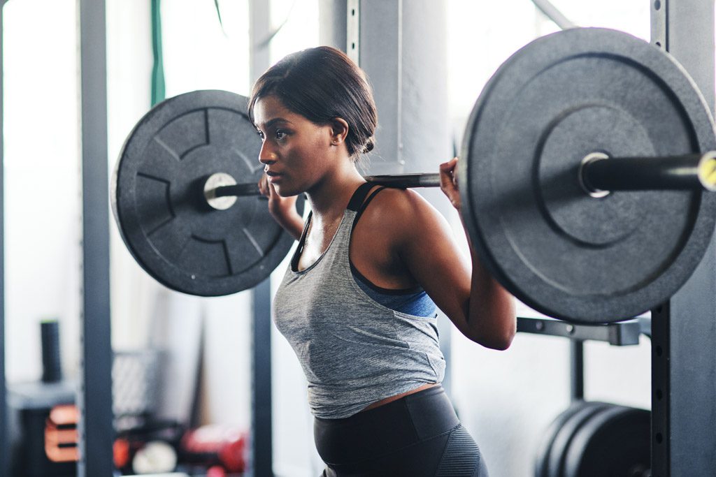 A woman performs a back squat workout in a gym.