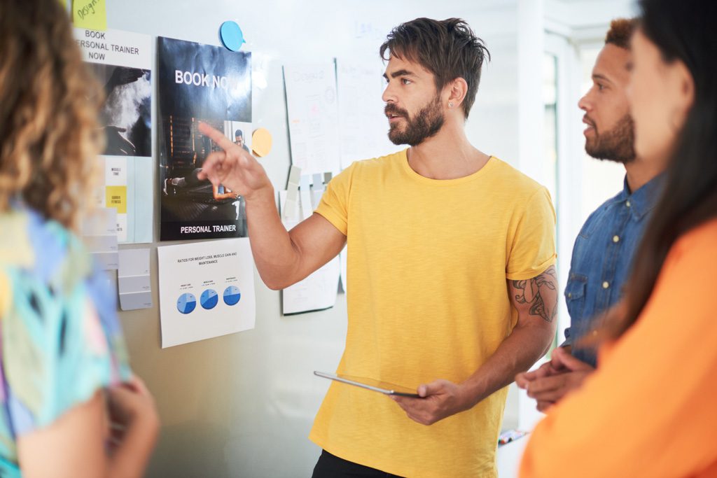 An entrepreneur goes over a gym marketing plan with his team in an office.