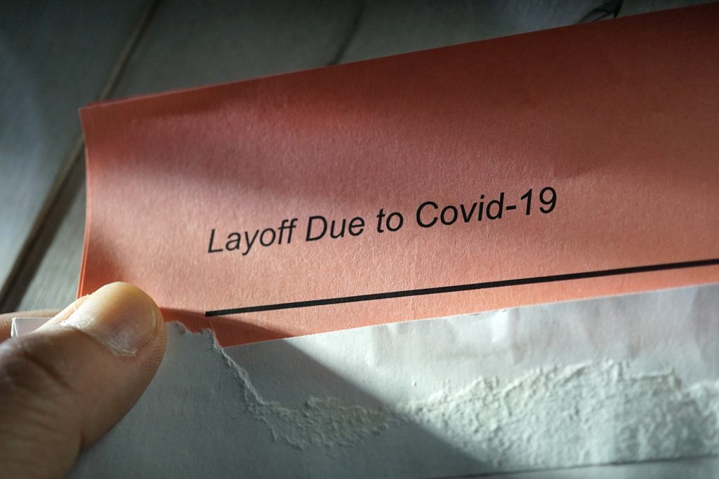 A close up of a hand holding a slip with a COVID-related layoff notice.