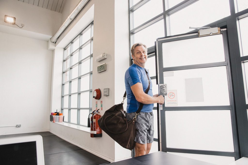 A gym's best client smiles as he walks out the door carrying his gym bag.