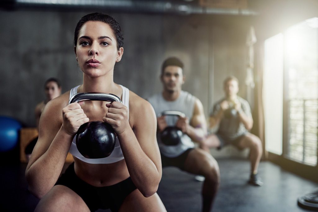 A number of fit people squat holding kettlebells in a group fitness class.