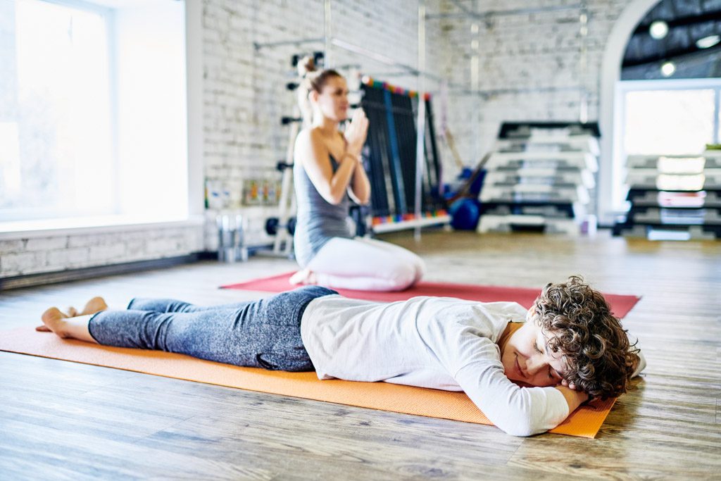 A smiling woman lies on her stomach on a mat as part of a "recovery class" at a gym.