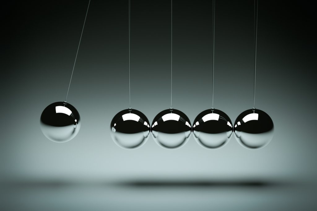 A closeup of the steel balls of a Newton's cradle, with one ball about to strike another.