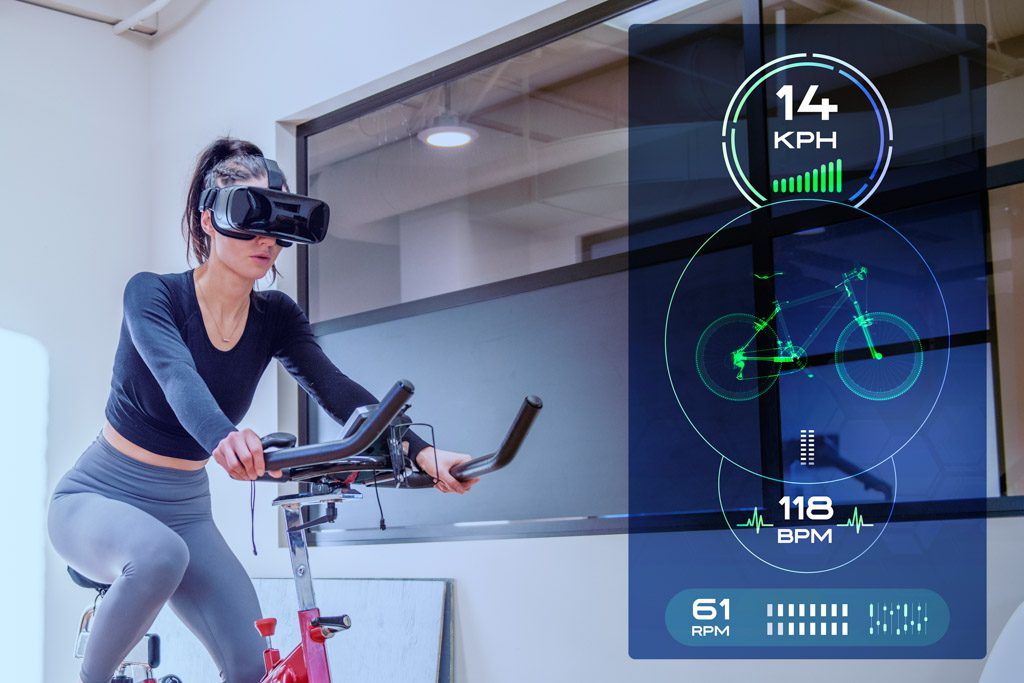 A woman rides a bike with a VR headset while wearable tech collects training info.