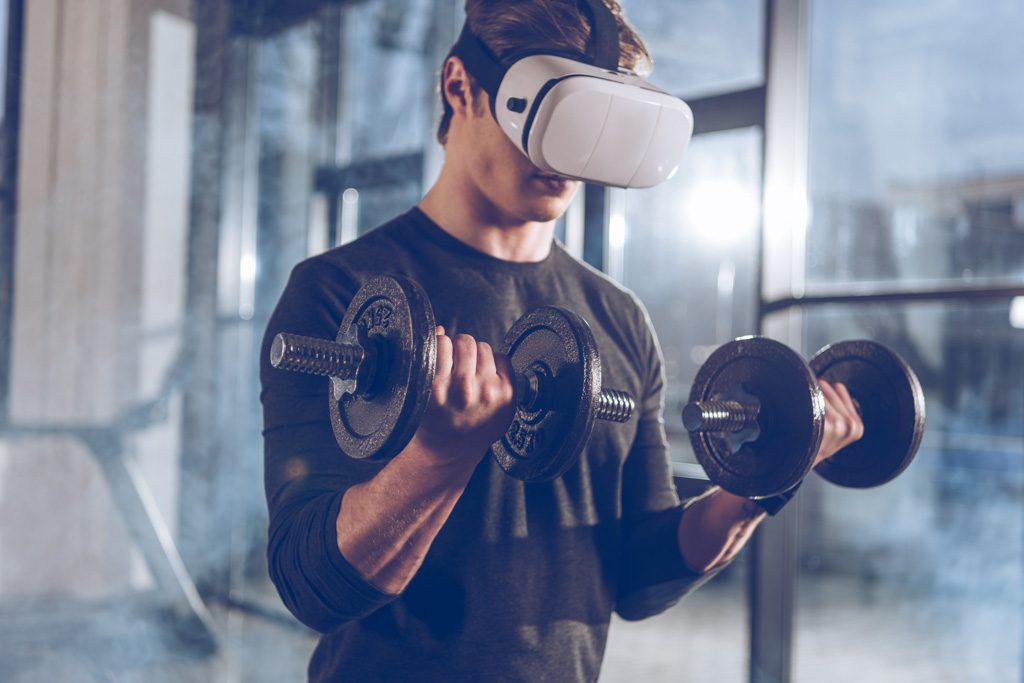 A man performs biceps curls with a VR headset to illustrate the fitness industry trend of using virtual coaching.