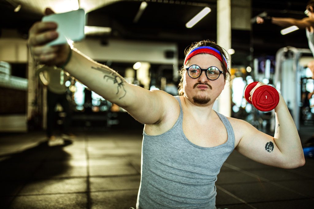 A gym owner poses comically with a red dumbbell to generate engagement on Facebook.