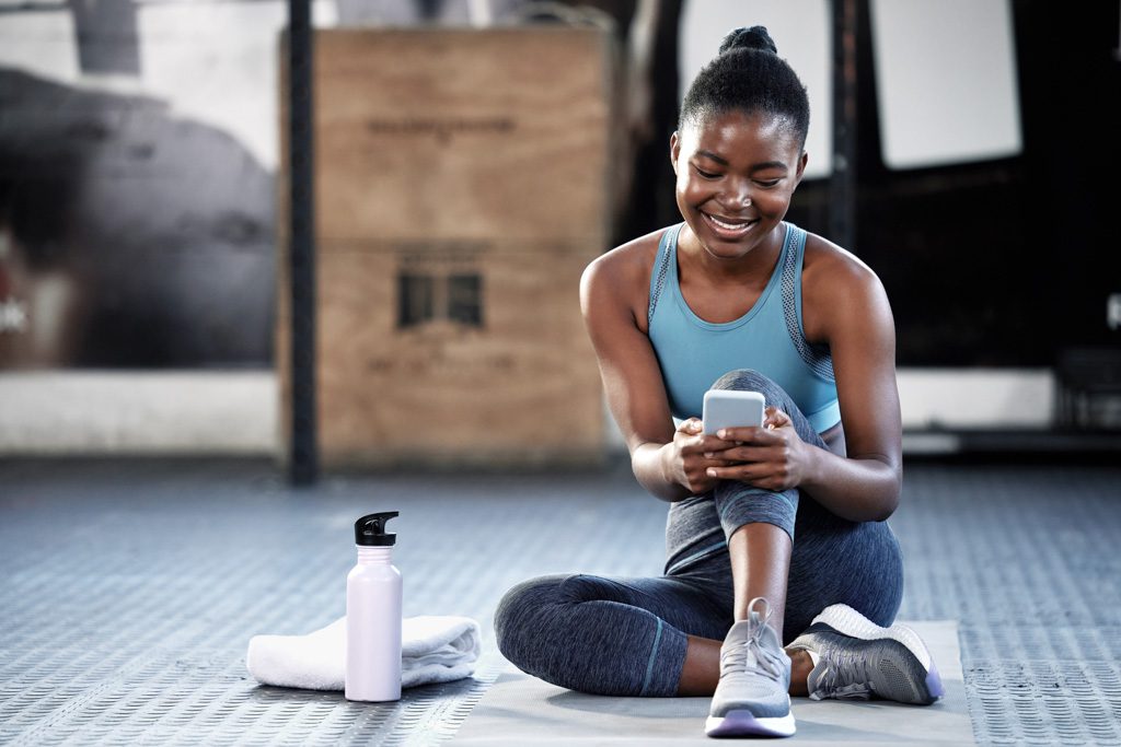 A smiling, athletic young woman engages with her gym's Facebook page.