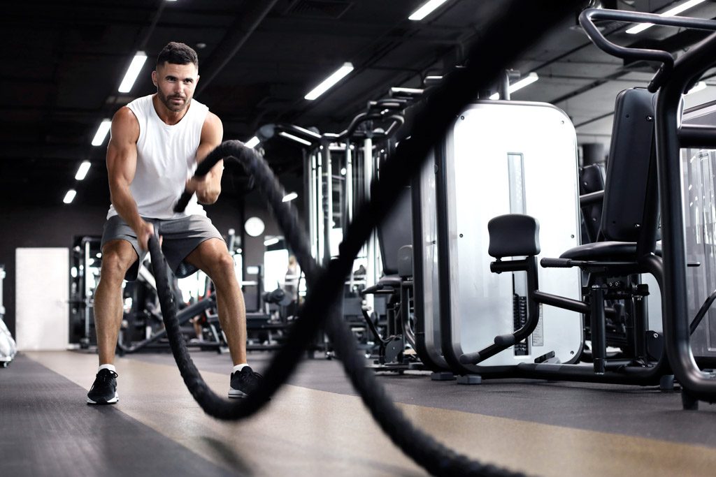 A man uses battle ropes in a gym.